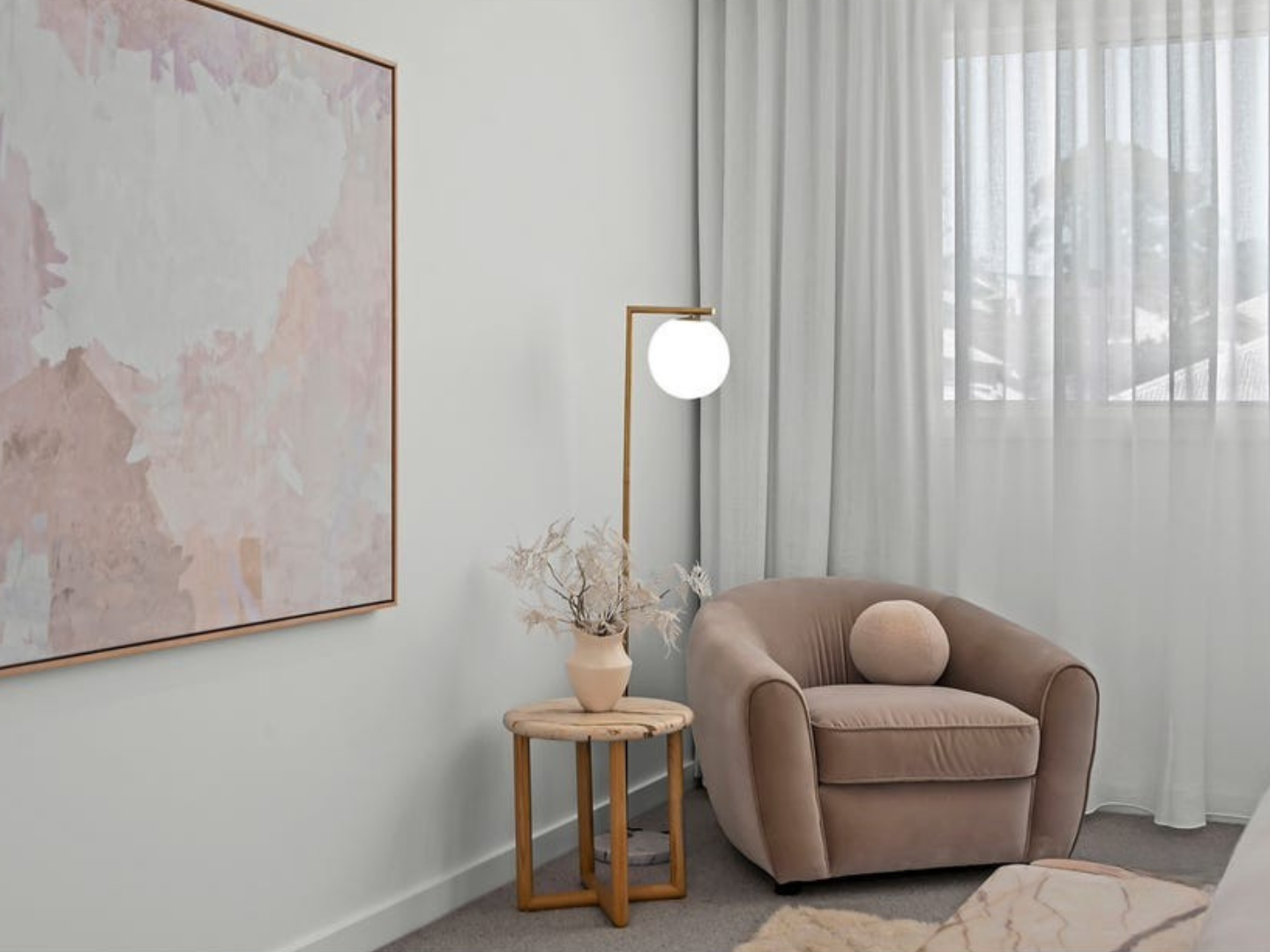 Modern living room with a beige armchair, side table, and abstract wall art hired for property styling