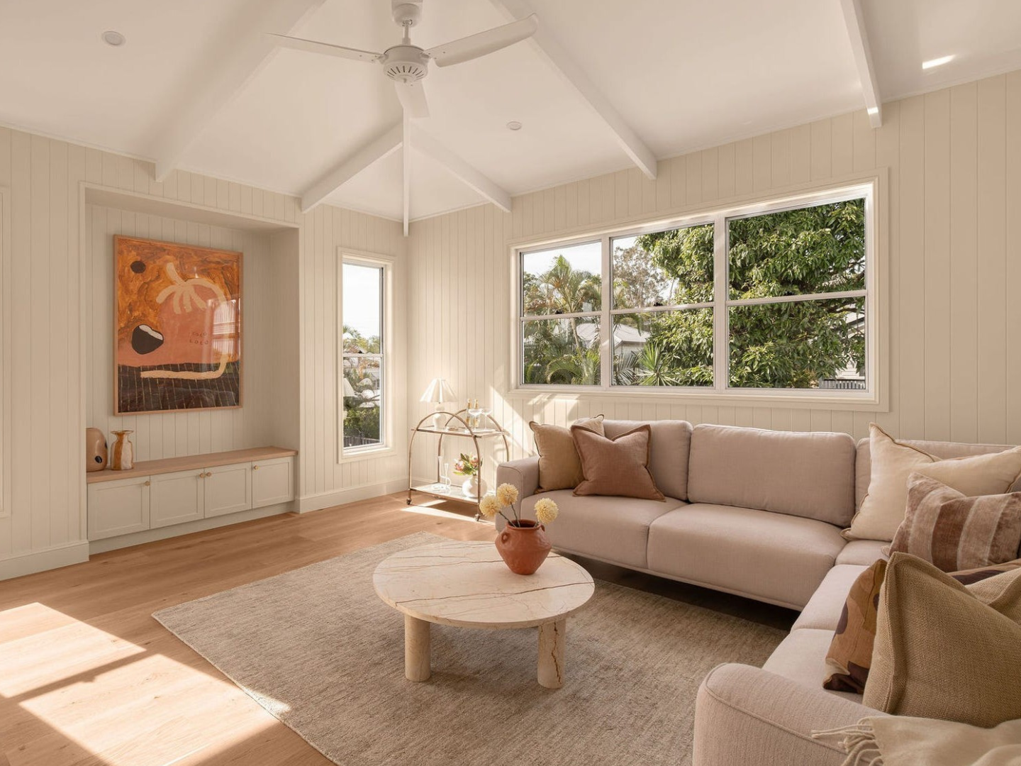Living room with beige sectional sofa, coffee table, and large window and artwork hired for property styling in Brisbane