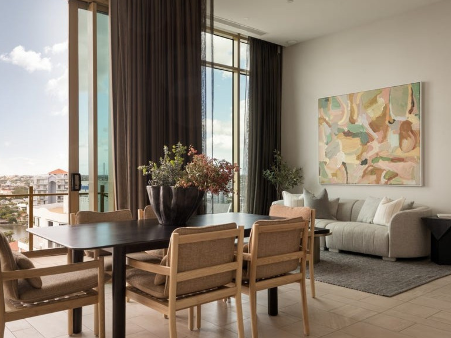 Modern living room with a dining table and chairs, large windows, and a colorful abstract painting hired for proeprty styling